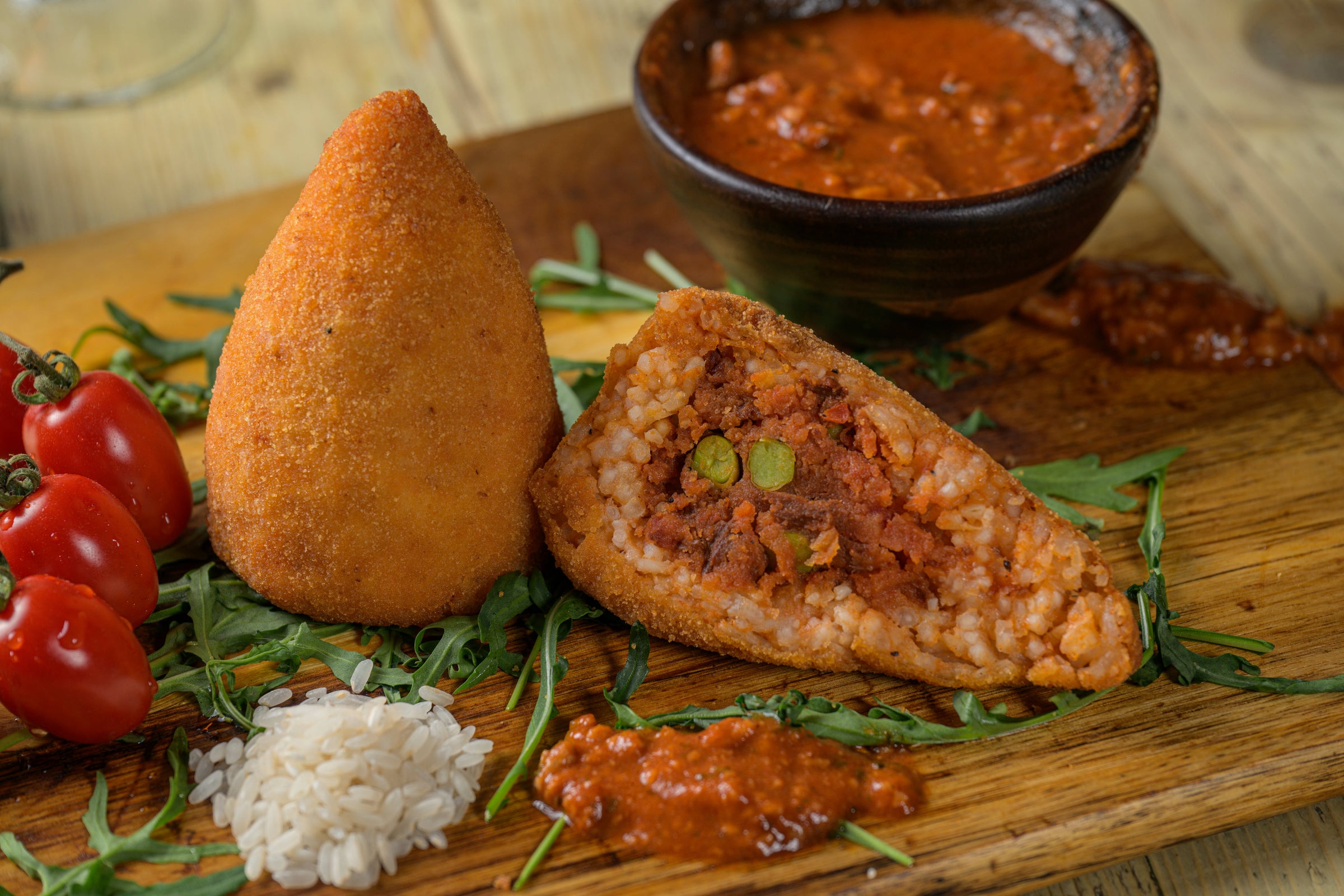 Arancini vegani siciliani artigianali Dolce&Vegano su tavolozza in legno, uno tagliato a metà con ripieno visibile